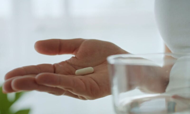 devojka drži tabletu na dlanu i čašu sa vodom u drugoj ruci